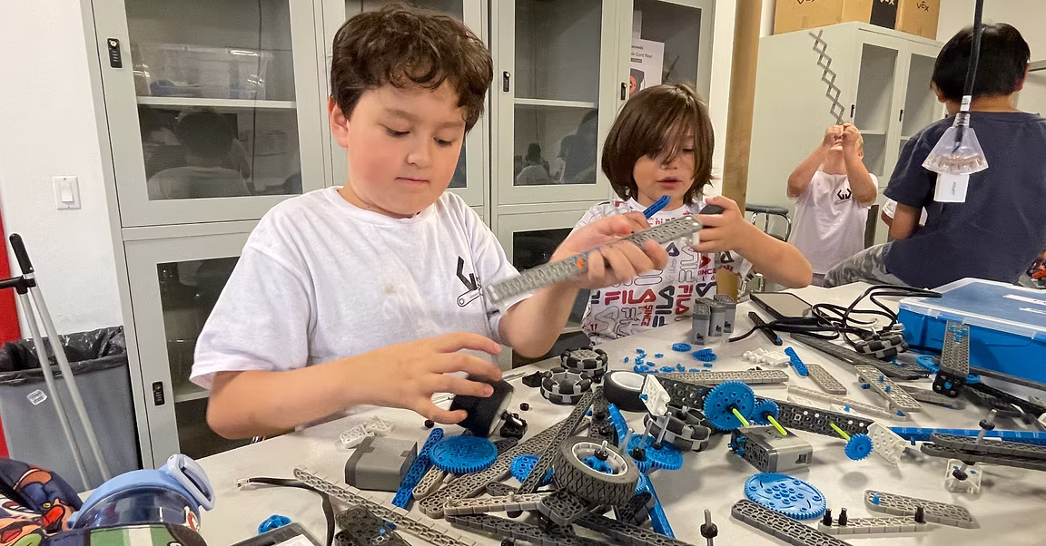 Campers building robots with VEX IQ parts spread across the bench